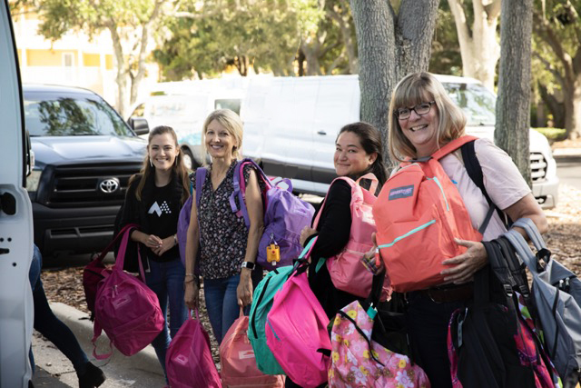 Associates smiling and holding backpacks while loading up a truck for the Backpack Drive.