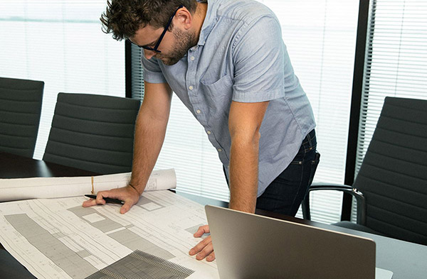 A man standing over his desk, reading through documents.