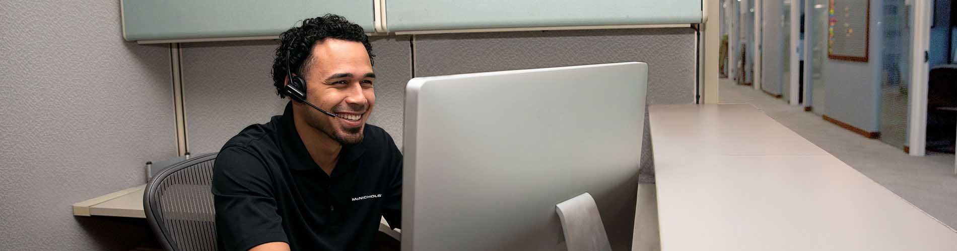 A photo of a smiling McNICHOLS Associate who is sitting at his desk and serving a customer over the phone.