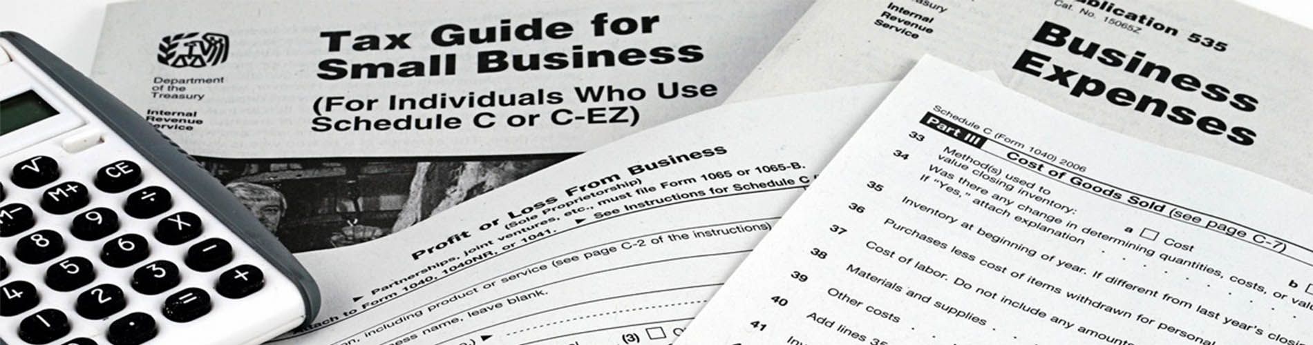 An image of several tax forms laying on top of each other and a calculator on the left.