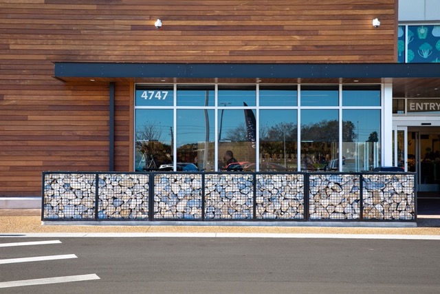 A short wall of rock-filled gabion baskets, aligned in front of windows outside Greenwise Market.