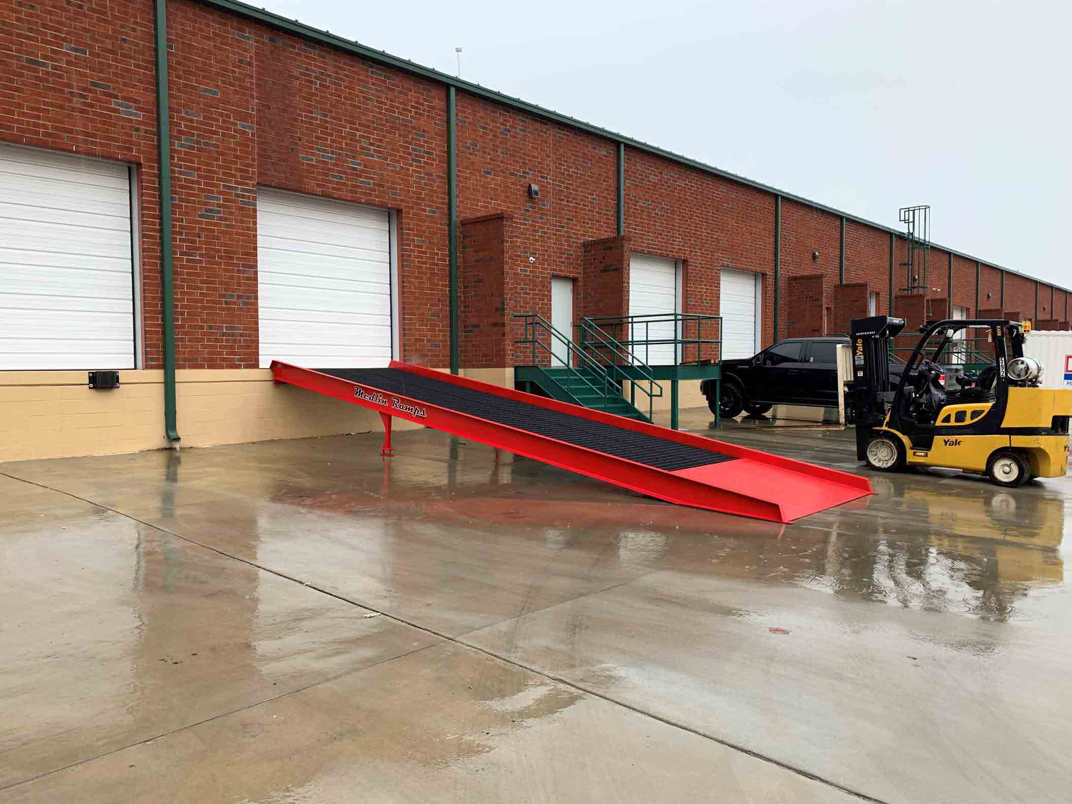 A black and red Medlin Ramps ramp used outside a warehouse.