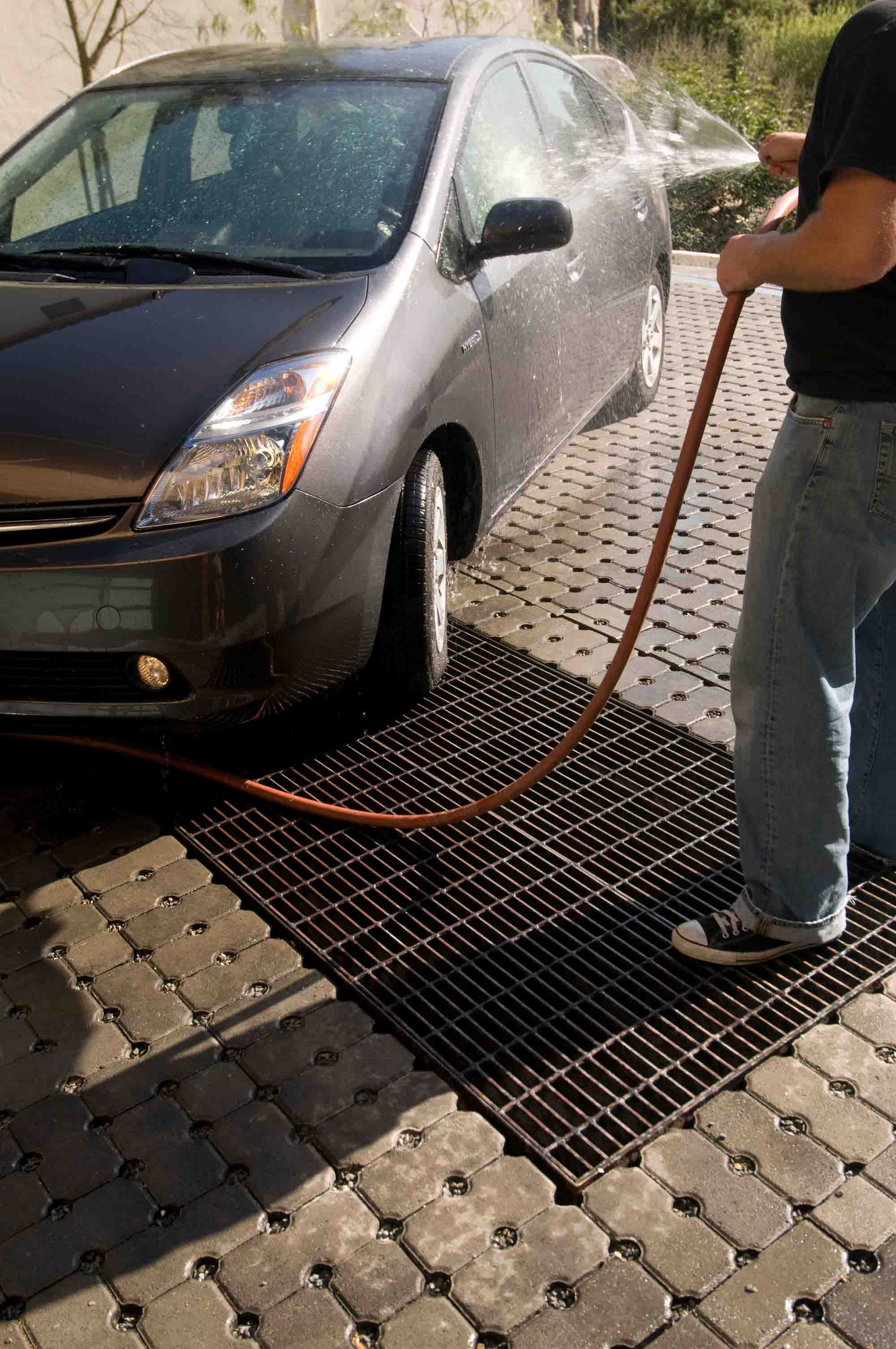 A car being sprayed down while sitting on top of McNICHOLS® Bar Grating, which is used as part of a rainwater recycling system.