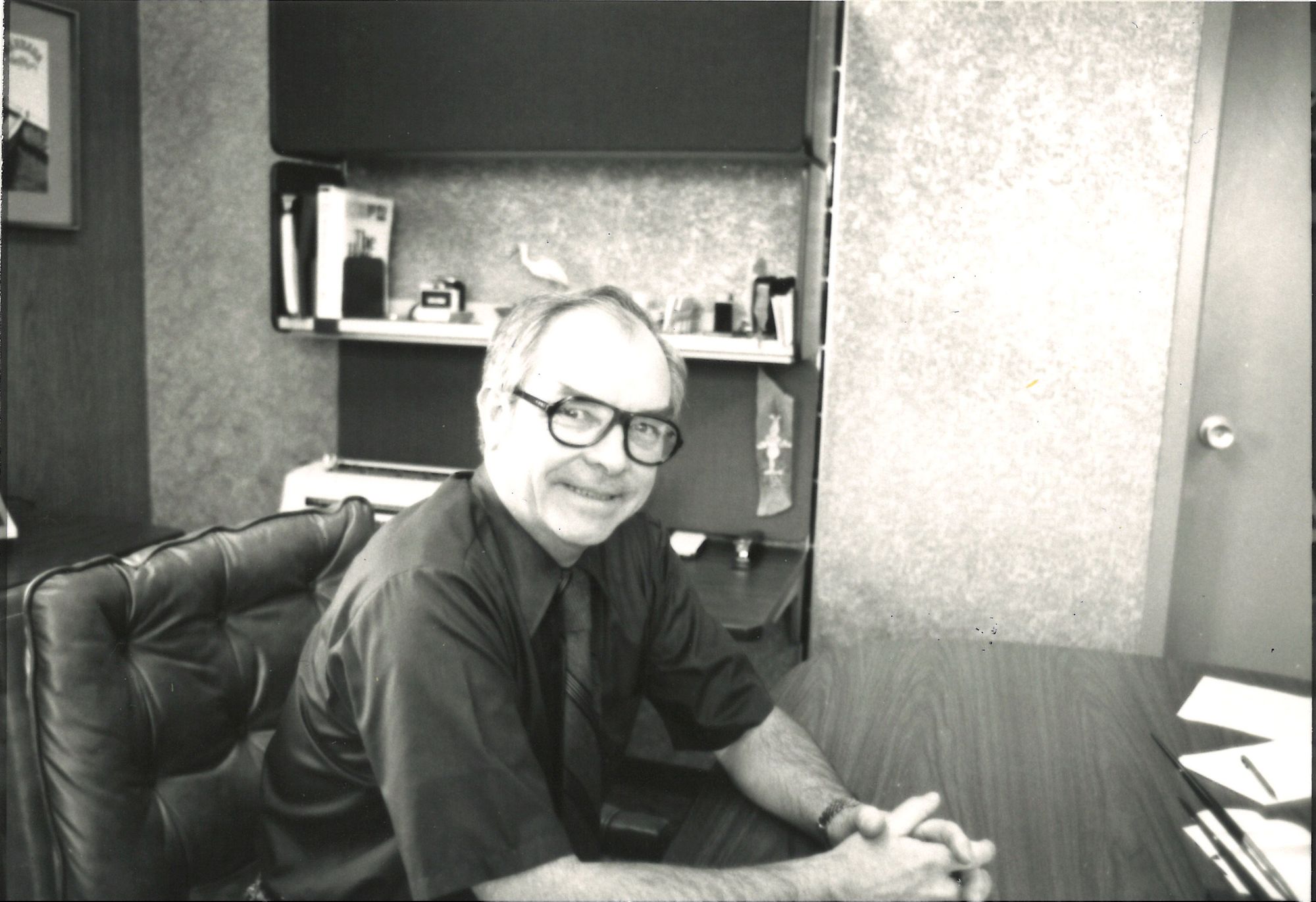 A black-and-white photo of Bob McNichols in the office, smiling.