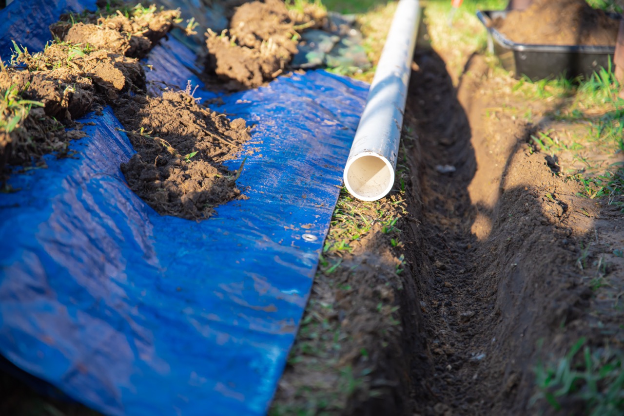 PVC pipes and blue tarp next to a dirt trench, ready for a Trench Grate or Drain System.