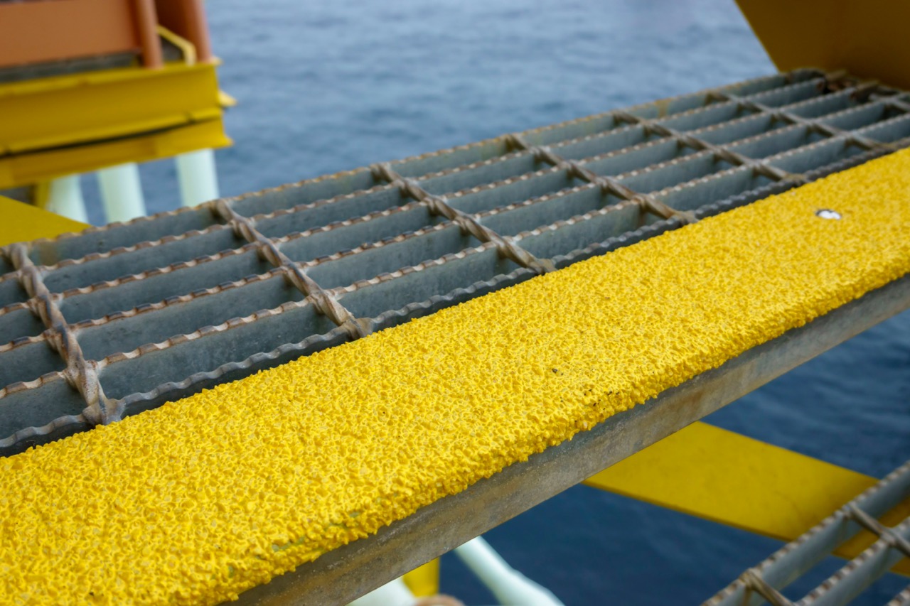 A close-up of a Bar Grating Stair Tread with yellow anti-slip nosing. The grated structure provides drainage and safety, commonly used in marine and industrial environments.