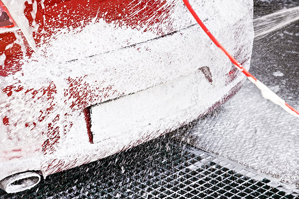 A picture of the back of a car covered in soap, with a Fiberglass Grating drain underneath.