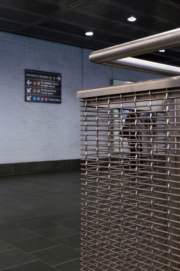 Close-up view at Fulton Street Subway Station in New York City showing stainless steel railing with Designer Mesh CHATEAU™ 3110 Infill Panels, with directional transit signage visible in the background.