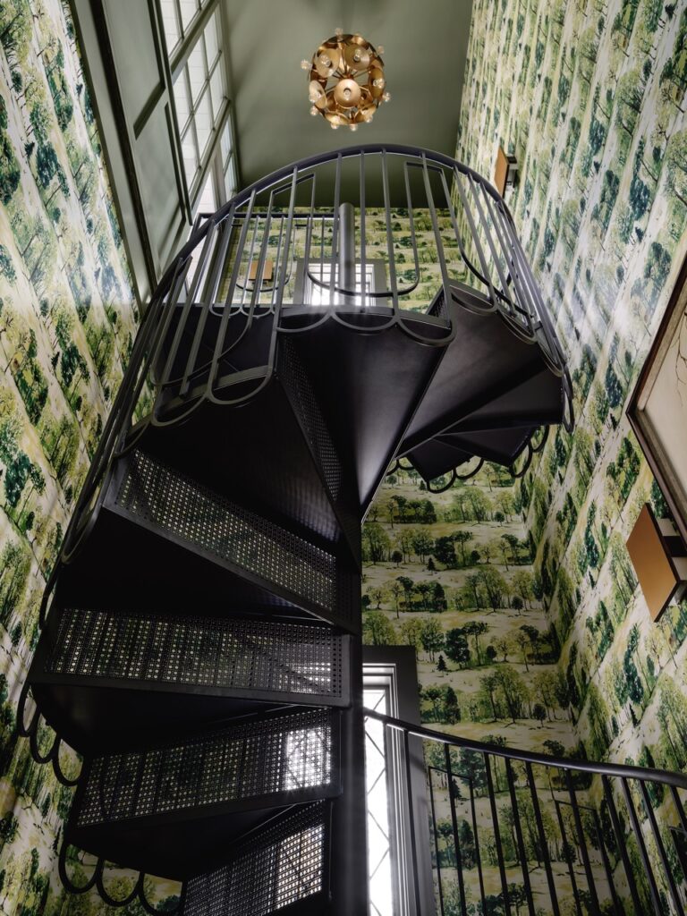 Interior spiral staircase with black metal steps featuring Designer Perforated, OCTAGON CANE 2036, set against patterned green wallpaper and a gold ceiling light.