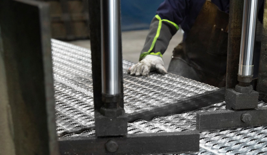 McNICHOLS associate pushes plank grating through a bandsaw.