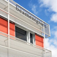 Building exterior with red panels and white framing, featuring Designer Mesh, AURA™ panels used as balcony and facade screening.