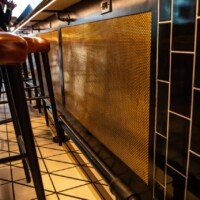 Modern bar with brown leather stools and a Bronze Designer Mesh, ASHLAND™ metal panel on the bar front.