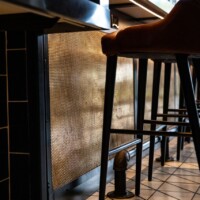 Modern bar with brown leather stools and a Bronze Designer Mesh, ASHLAND™ metal panel on the bar front.