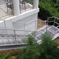 Smooth Standard-Duty Welded Bar Grating Stair Treads on an exterior metal staircase wrapping around a building with guardrails and landscaping below.