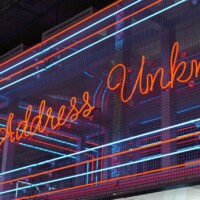 “Address Unknown” neon sign mounted on Square Wire Mesh sheet that is Welded and Stainless Steel with red and blue lighting at POST Market Houston.