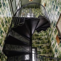 Interior spiral staircase with black metal steps featuring Designer Perforated, OCTAGON CANE 2036, set against patterned green wallpaper and a gold ceiling light.