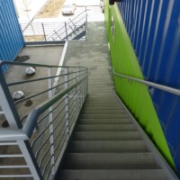 Elevated stair and landing at The Box Office building with TRACTION TREAD™ Plank Grating stair treads and flooring between colorful container structures.
