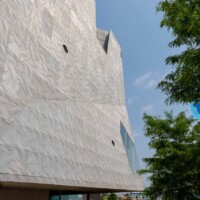 Street-level view of Designer Expanded Metal, Flattened LANCET™ 31651-F facade at Walker Art Center in Minneapolis, MN, showing the textured exterior above a pedestrian walkway with trees and people below.