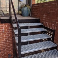 Exterior staircase with Serrated Standard-Duty Welded Bar Grating Stair Treads and metal handrail leading to a residential entry.
